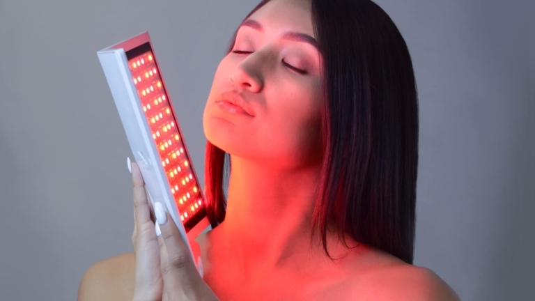 A woman holding a red light device up to her face